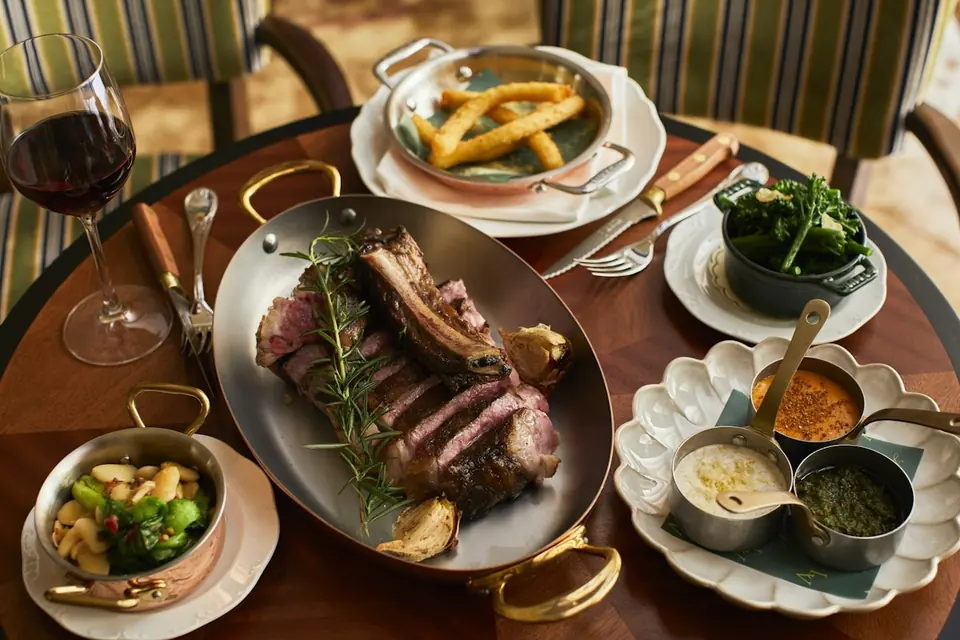 Steak, sides and a glass of red wine on a table at Locanda Verde