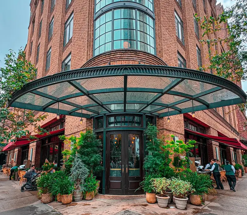 The corner entrance to Locanda Verde, framed by plants under a glass canopy